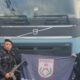 Dois policiais militares com fuzil e bandeira PMERJ em frente a caminhão Volvo azul