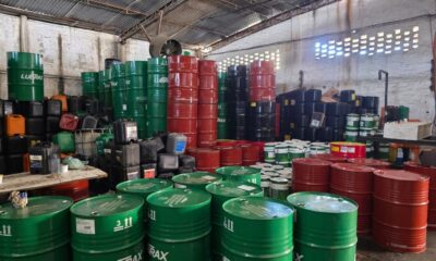 Armazém com pilhas de tambores verdes, vermelhos e pretos, além de galões e embalagens diversas