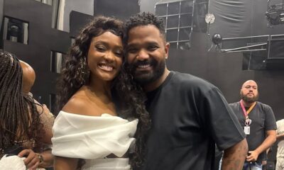 Erika Januza e Arlindinho sorrindo e abraçados em um estúdio com fundo escuro