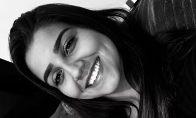 Close-up em preto e branco de mulher jovem sorrindo, com cabelo escuro e piercing no nariz