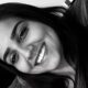 Close-up em preto e branco de mulher jovem sorrindo, com cabelo escuro e piercing no nariz