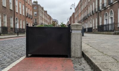 Fotografia realista de uma bicicleta como único protagonista visual diante de uma barreira metálica estreita em uma via compartilhada de Dublin, demonstrando concretamente a dificuldade de passagem causada pela infraestrutura urbana, sem pessoas e sem textos visíveis.