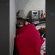 Homem deitado em cama, coberto por edredom vermelho, dormindo em quarto com aparelho de som
