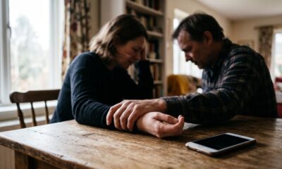 Um casal deprimido de cabeça baixa sentado à mesa de madeira com um smartphone e as mãos dadas.