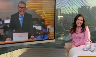Hélter Duarte na tela e Sabina Simonato rindo em estúdio, com laptop e vista urbana