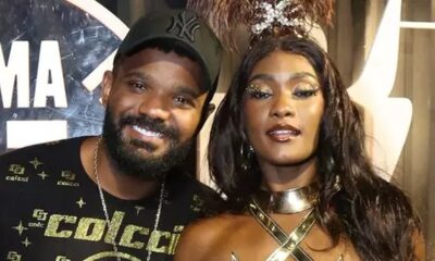 Erika Januza e Arlindinho sorrindo, ele de boné, ela com maquiagem dourada e roupa de festa