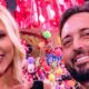 Homem e mulher sorrindo em evento festivo com fundo colorido