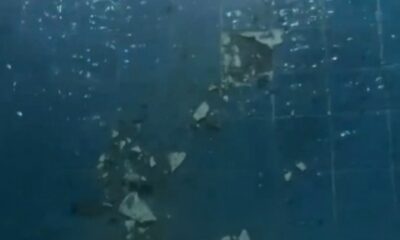 Piscina azul com azulejos danificados e detritos brancos após explosão