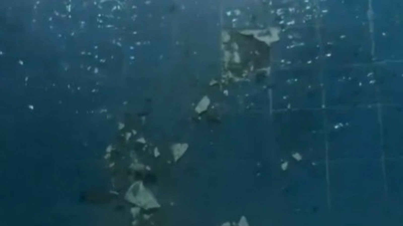 Piscina azul com azulejos danificados e detritos brancos após explosão