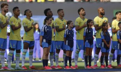 Jogadores de futebol de camisa amarela e crianças mascotes em campo