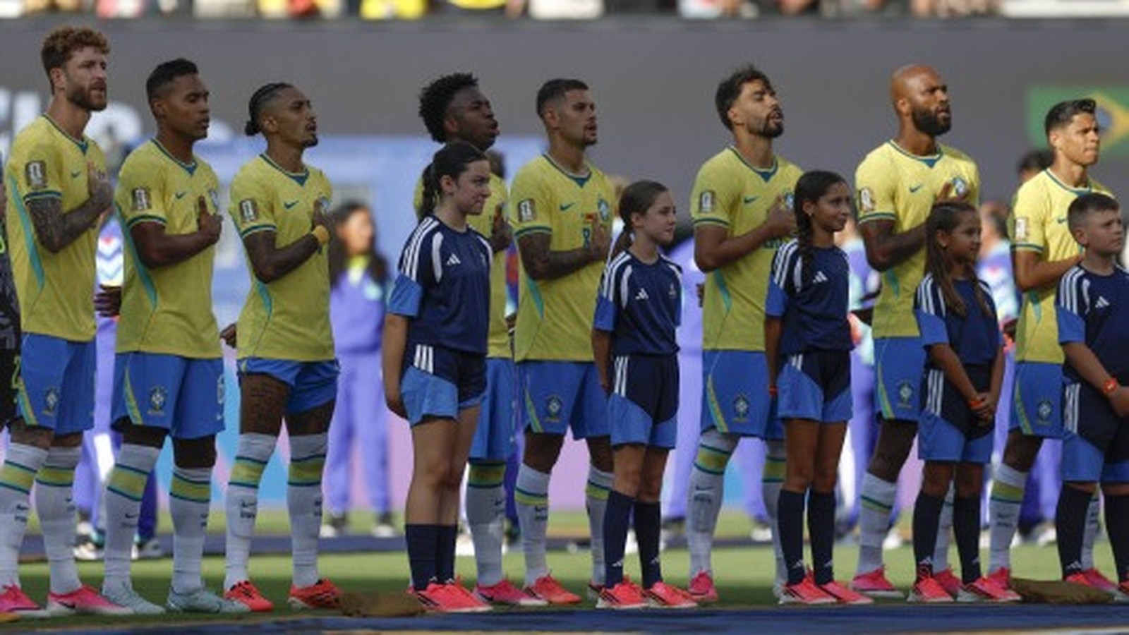 Jogadores de futebol de camisa amarela e crianças mascotes em campo