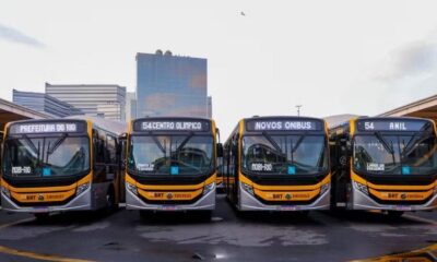 Quatro ônibus BRT novos amarelos e cinzas, com letreiros 'MOBI-RIO' e '54 ANIL'