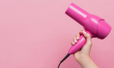 Mão segurando um secador de cabelo rosa brilhante contra um fundo rosa claro