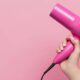 Mão segurando um secador de cabelo rosa brilhante contra um fundo rosa claro