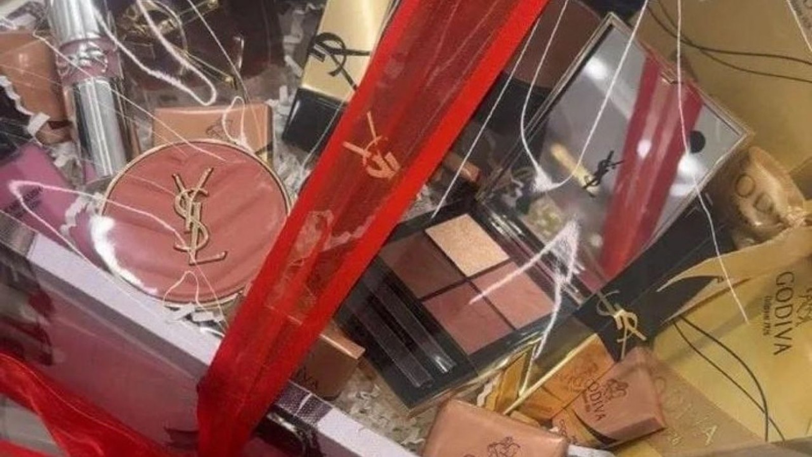 Maquiagens YSL e chocolates Godiva em cesta de presente com fita vermelha