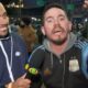 Repórter sorrindo segura microfone da Band e torcedor gesticula. Texto 20:00 Jornal da Band