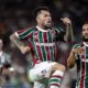 Jogador do Fluminense com barba e tatuagens celebra em campo durante partida noturna