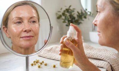 Mulher madura em frente ao espelho segurando um hidratante facial, com a pele visivelmente hidratada, luminosa e de aparência saudável em um banheiro bem iluminado
