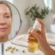 Mulher madura em frente ao espelho segurando um hidratante facial, com a pele visivelmente hidratada, luminosa e de aparência saudável em um banheiro bem iluminado