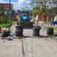 Barricada de pneus empilhados em rua, com retroescavadeira azul ao fundo e lixo