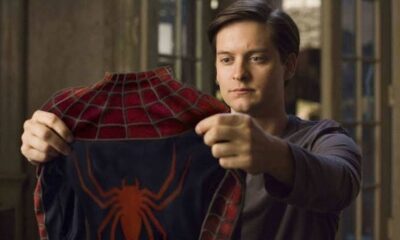 Tobey Maguire segura o traje do Homem-Aranha vermelho e azul, olhando para ele