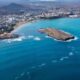 Vista aérea de cidade costeira em Cabo Verde com oceano azul, ilha rochosa e montanhas.