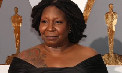 Whoopi Goldberg, dreadlocks, vestido preto, tatuagem, fundo com silhuetas douradas de Oscar