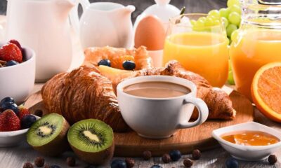 Mesa com café da manhã variado: croissants, café, suco de laranja, frutas, ovo e geleia.