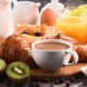 Mesa com café da manhã variado: croissants, café, suco de laranja, frutas, ovo e geleia.