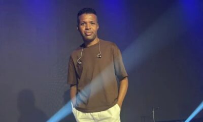 Cantor Diogo Nascimento no palco, camiseta marrom, fones de ouvido no pescoço