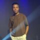 Cantor Diogo Nascimento no palco, camiseta marrom, fones de ouvido no pescoço