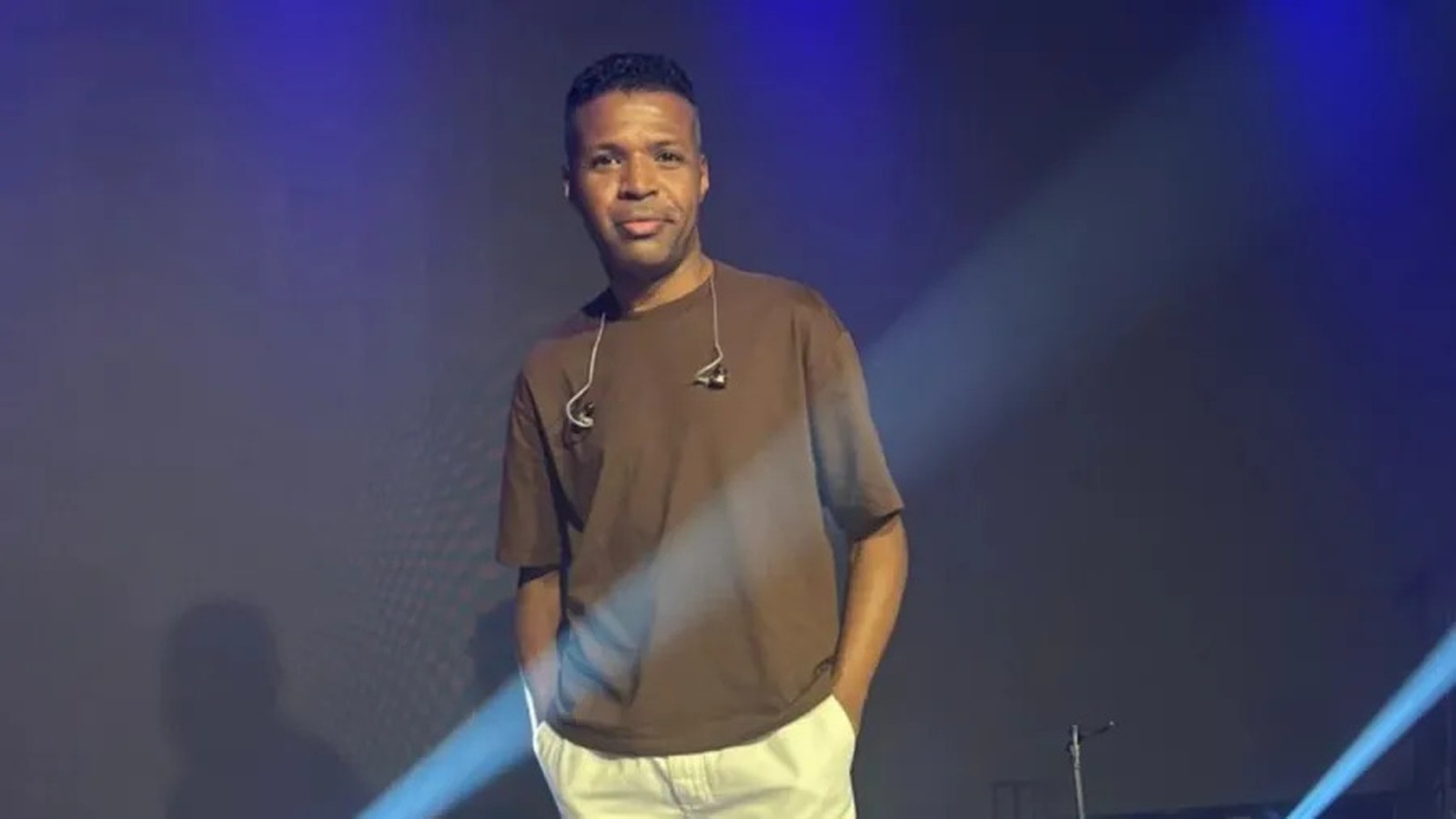 Cantor Diogo Nascimento no palco, camiseta marrom, fones de ouvido no pescoço