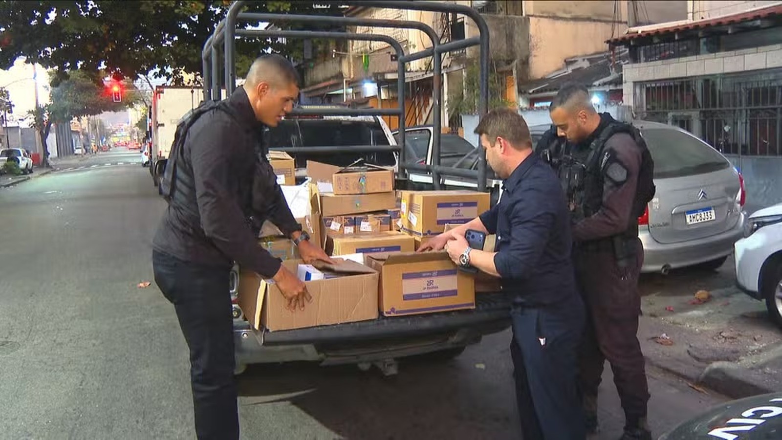 Três homens inspecionam caixas de papelão na caçamba de caminhonete em rua