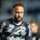 Neymar de barba e cabelo encaracolado, vestindo camisa Umbro do Santos FC com patrocinadores