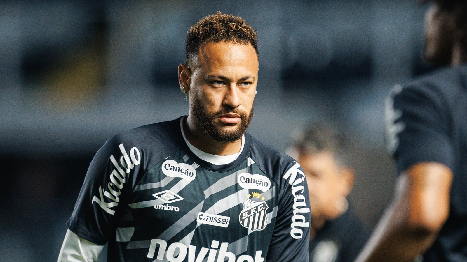 Neymar de barba e cabelo encaracolado, vestindo camisa Umbro do Santos FC com patrocinadores