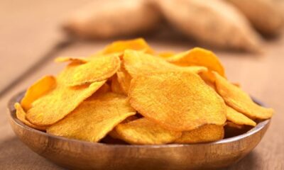 Tigela de madeira cheia de chips alaranjados de batata-doce em uma mesa de madeira.