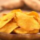 Tigela de madeira cheia de chips alaranjados de batata-doce em uma mesa de madeira.