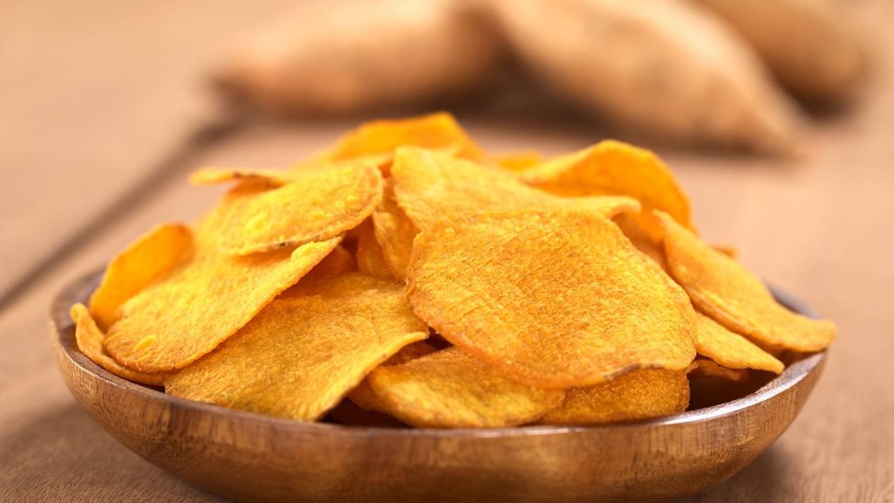 Tigela de madeira cheia de chips alaranjados de batata-doce em uma mesa de madeira.