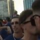 Close-up de dois homens com óculos escuros, um beijando o outro no rosto em meio à multidão