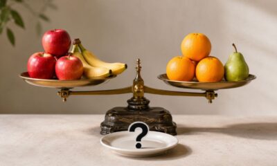 Balança de pratos equilibrada com maçãs, bananas, laranjas e pera em quantidades diferentes, com um prato à frente exibindo uma interrogação.