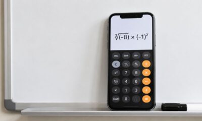 Celular com calculadora aberta sobre quadro branco, mostrando a expressão ∛(-8) × (-1)² sem resultado final.