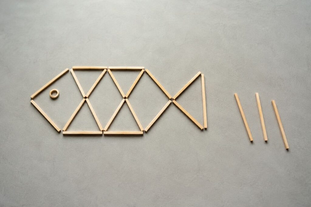 Montagem de peixe feita com palitos de madeira sobre fundo neutro, com três palitos reposicionados para mostrar a inversão do sentido do peixe no desafio visual.