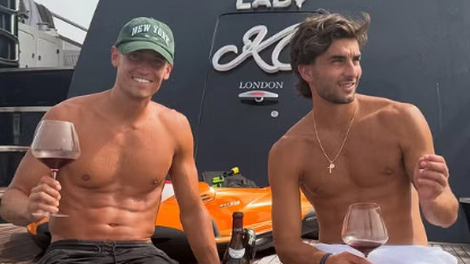 Dois homens sem camisa em barco, segurando taças de vinho, com inscrição "LADY M LONDON"