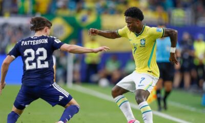 Vini Jr. (camisa 7, Brasil) em ação contra Patterson (camisa 22) em campo de futebol.