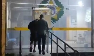 Dois homens, por trás, sobem escadas para porta de vidro com emblema policial