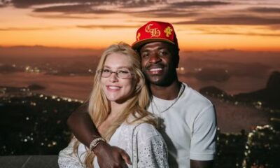 Homem e mulher sorrindo, abraçados, cidade ao pôr do sol, homem com relógios no pulso