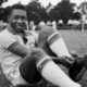 Jovem Pelé, sorrindo e sentado no gramado, ajusta chuteira com uniforme CBD