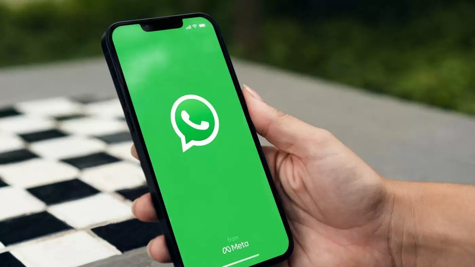 Mão segurando smartphone exibindo a tela inicial do aplicativo WhatsApp com logo e 'from Meta'