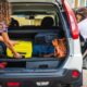 Duas mulheres arrumando malas no porta-malas de um carro branco para uma viagem