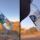 Mão enluvada segurando garrafa de água congelando sobre paisagem árida sob céu azul